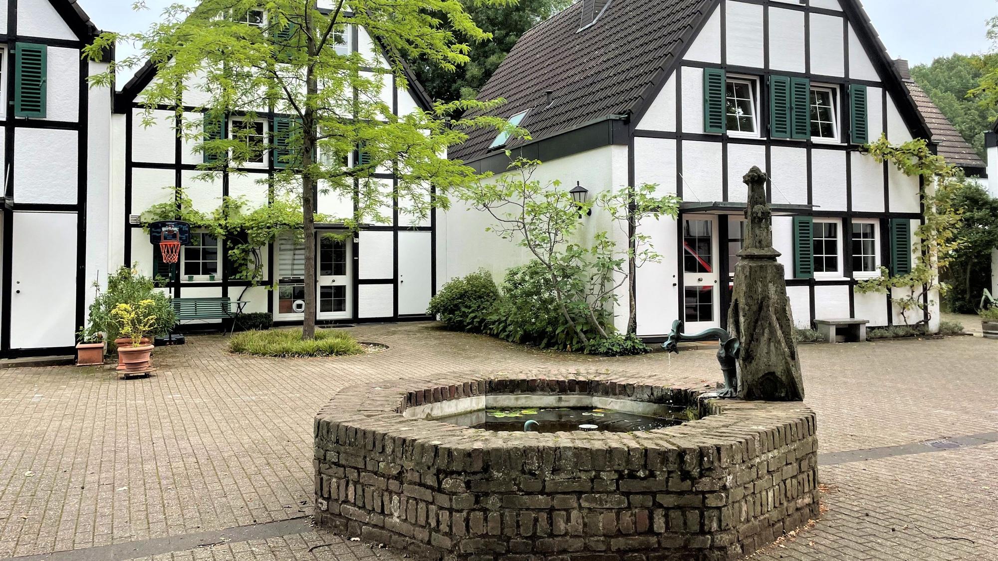 Ein Brunnen steht auf einem Platz vor zwei Häusern.