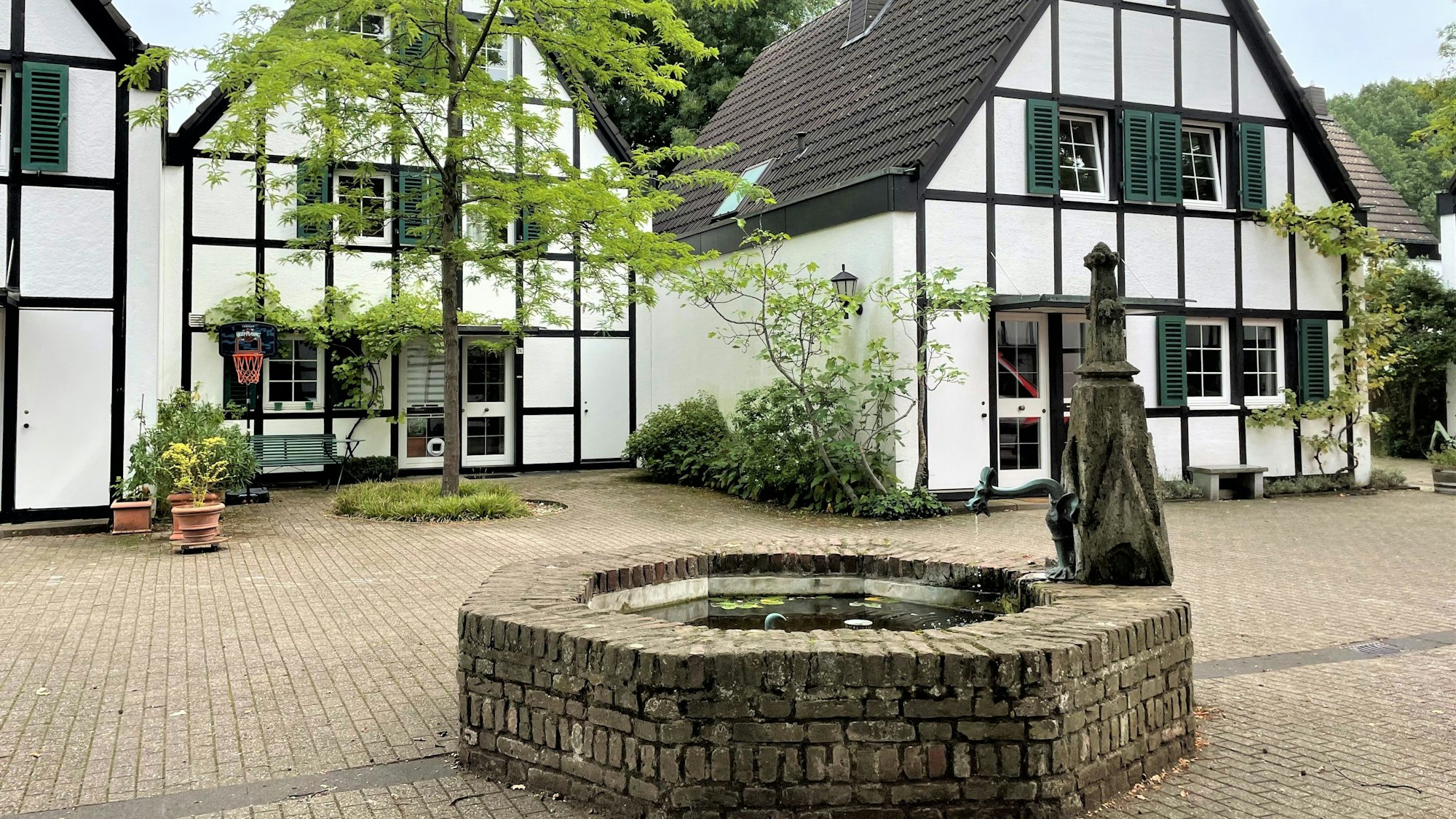 Ein Brunnen steht auf einem Platz vor zwei Häusern.