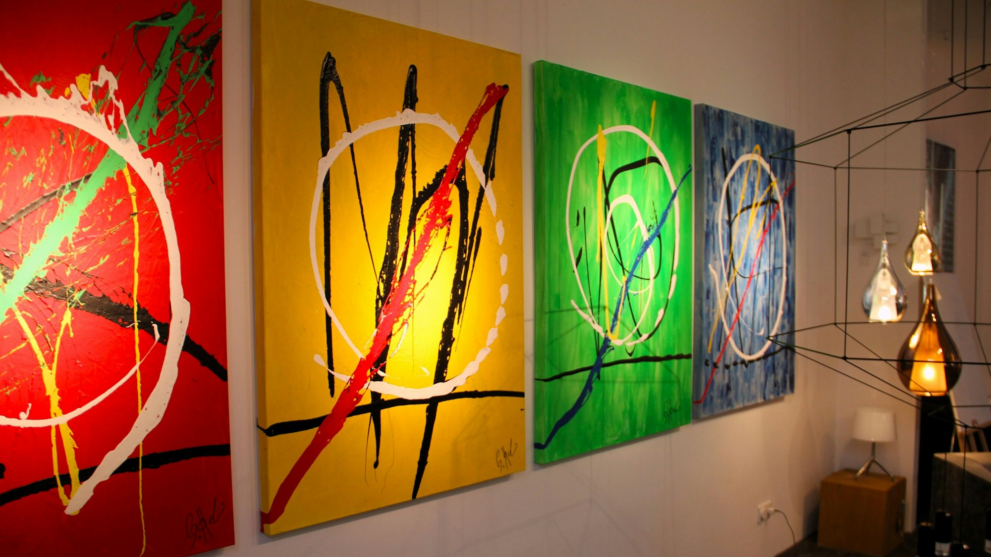 Vier bunte Bilder von Gerrit Hodemacher hängen an einer Wand nebeneinander.