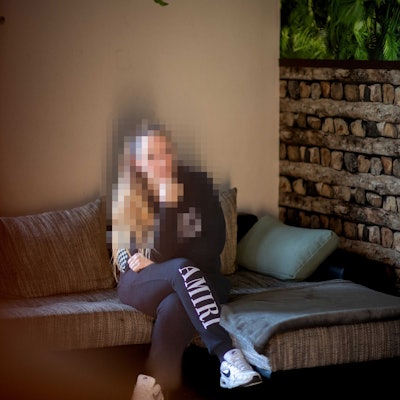 Das Bild zeigt Nadine Schäfer, wie sie auf einem Sofa sitzt. Ihr Gesicht ist zu ihrem Schutz gepixelt.