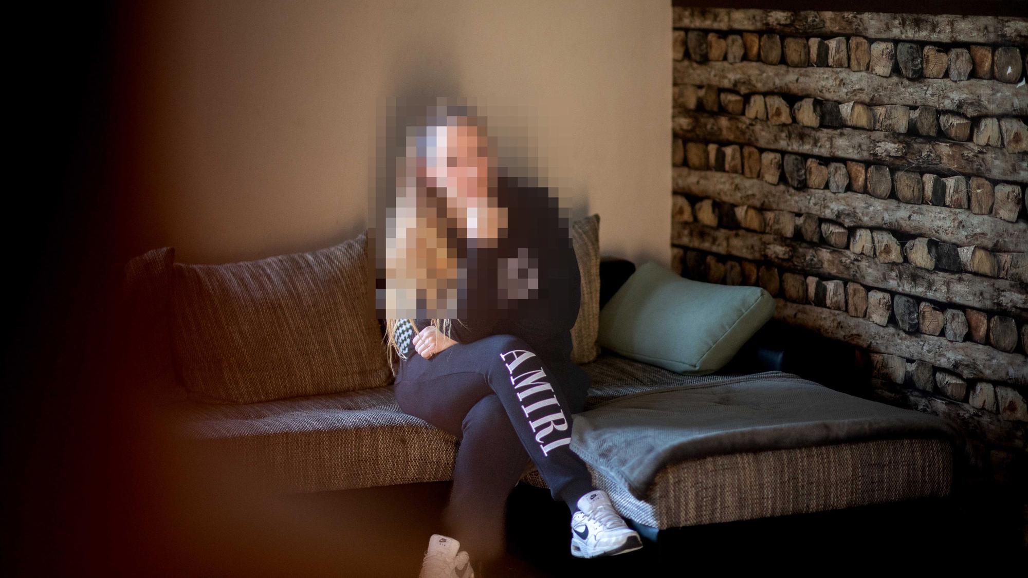 Das Bild zeigt Nadine Schäfer, wie sie auf einem Sofa sitzt. Ihr Gesicht ist zu ihrem Schutz gepixelt.