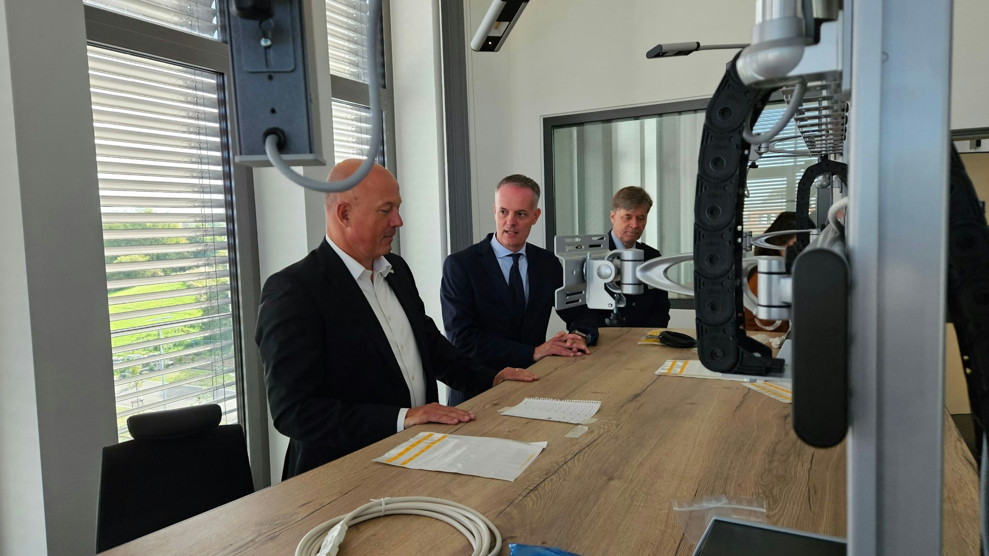 Drei Männer stehen an einem Schreibtisch.