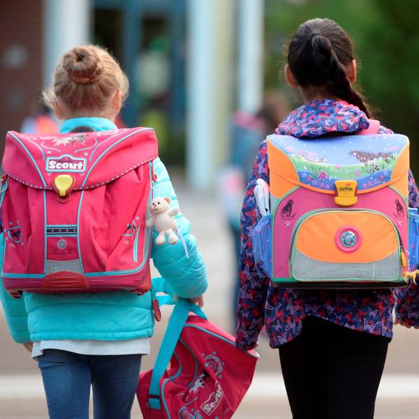 Drei Schülerinnen laufen mit ihren Schulranzen zur Schule. Die Gesichter der Kinder sind weg von der Kamera gewandt. (Archivbild)