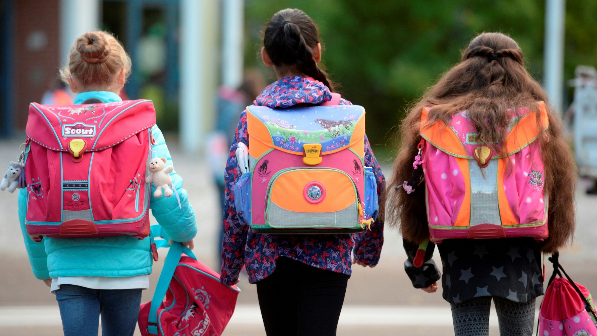 Drei Schülerinnen laufen mit ihren Schulranzen zur Schule. Die Gesichter der Kinder sind weg von der Kamera gewandt. (Archivbild)