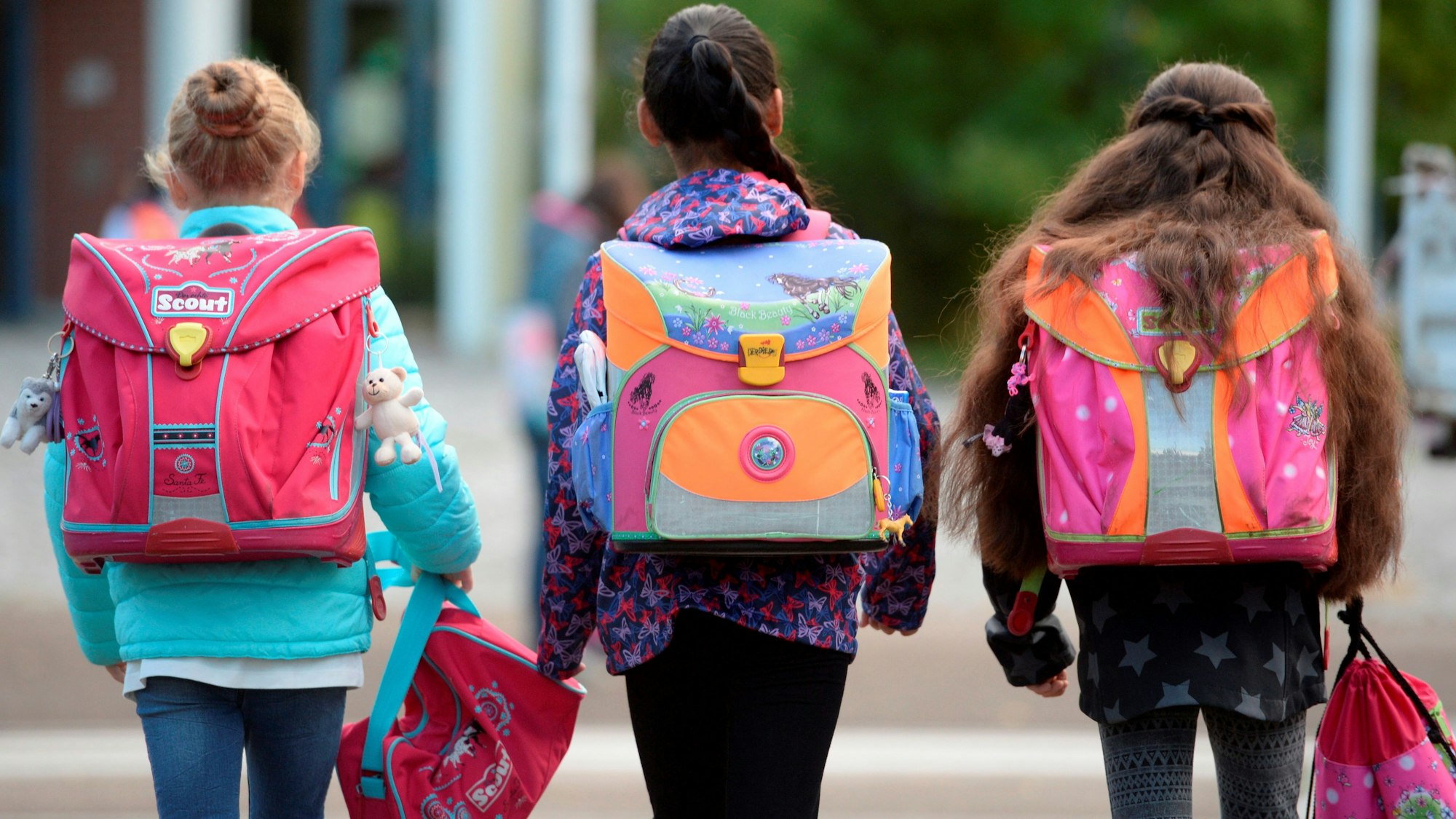 Das Symbolbild zeigt drei Kinder mit ihren Schulranzen auf dem Rücken.