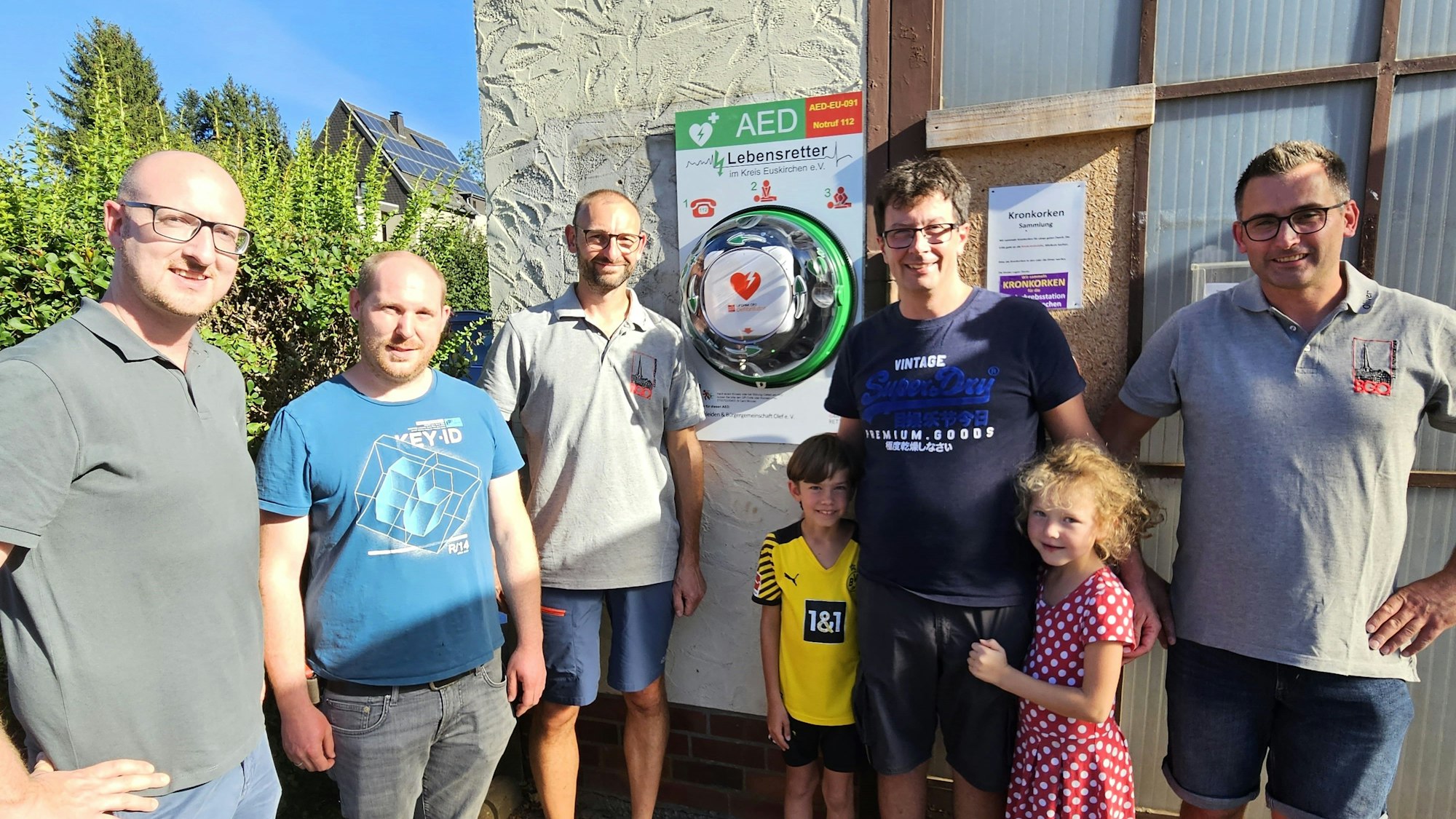 Um den Defibrillator stehen von links Ingo Pfennings, Christian Larres, Stefan Groß, Jesko Priewe mit Tochter und Sohn sowie Oliver Müller.
