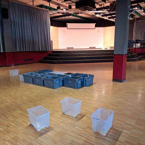 Auf dem Fußboden der gesperrten Aula des Kopernikus-Gymnasiums stehen rund ein Dutzend Plastikbehälter, die das Wasser auffangen, das durch das Flachdach ins Gebäude eindringt.