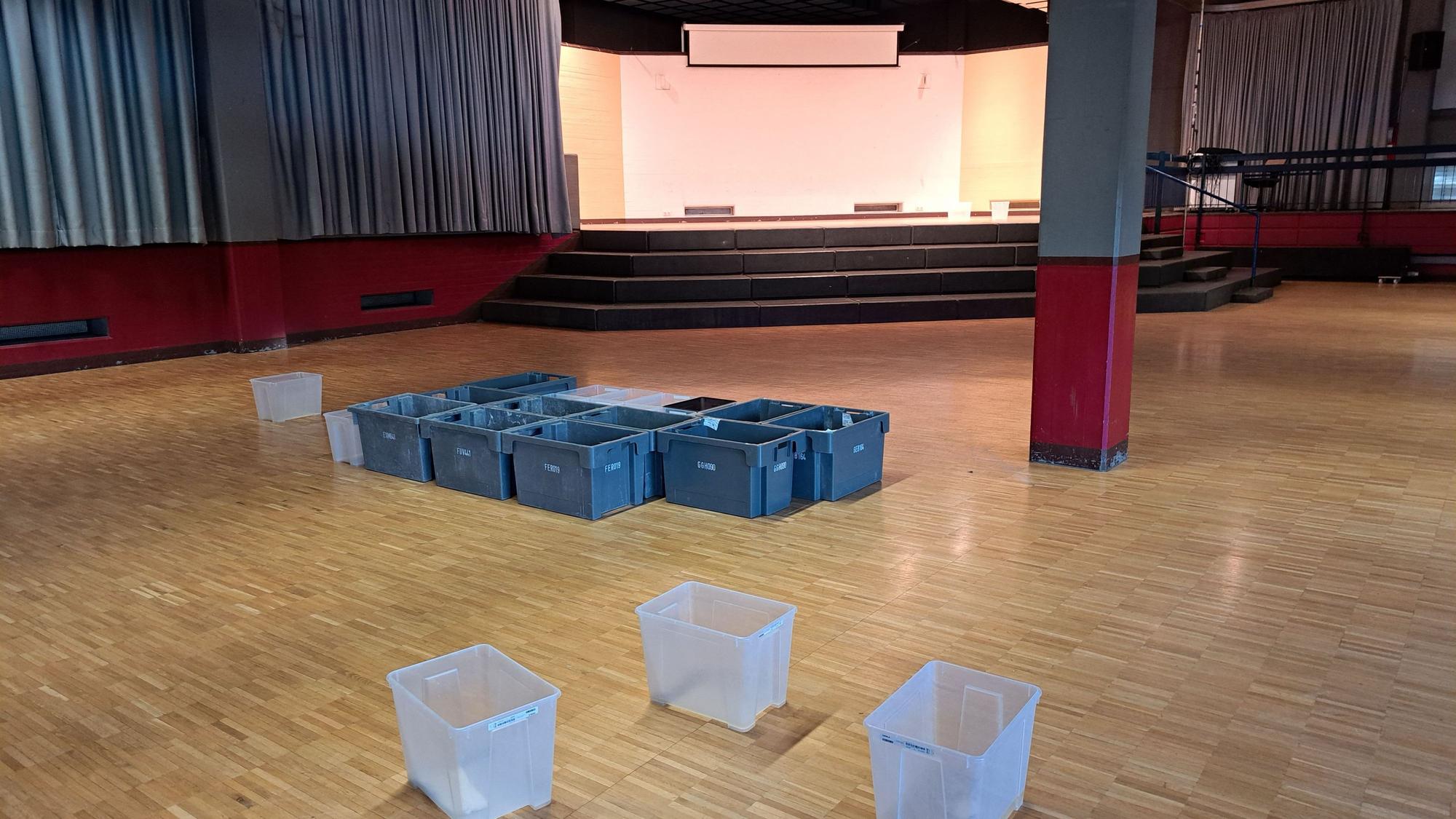 Auf dem Fußboden der gesperrten Aula des Kopernikus-Gymnasiums stehen rund ein Dutzend Plastikbehälter, die das Wasser auffangen, das durch das Flachdach ins Gebäude eindringt.