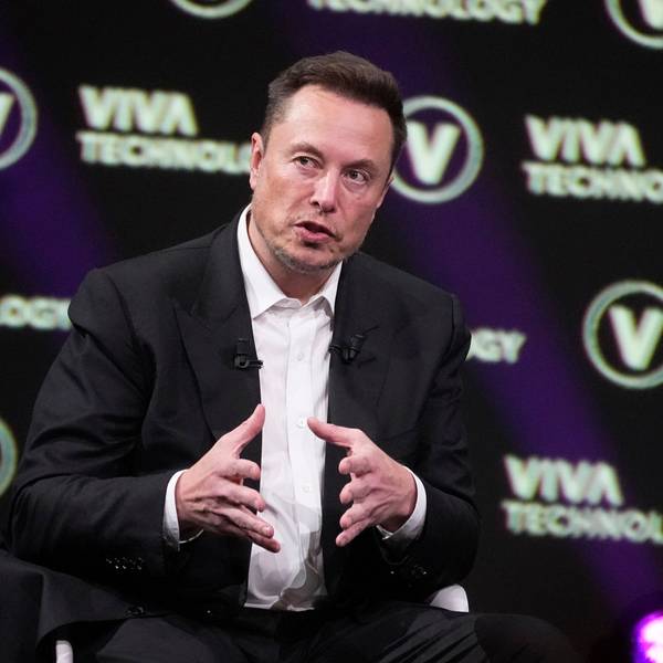Elon Musk im Anzug und Hemd vor einer Leinwand mit der Aufschrift "Viva Technology"