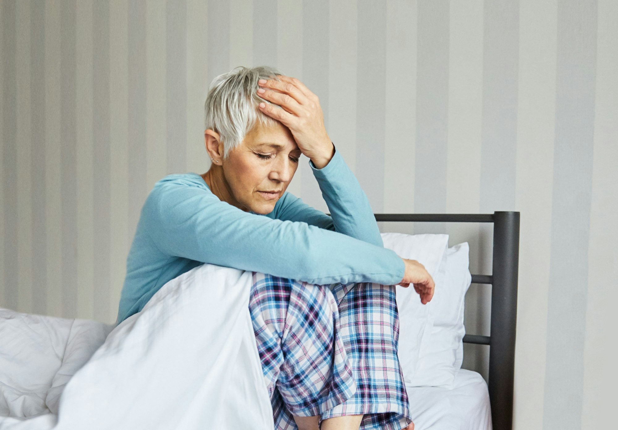 Portrait of an upset and unhappy senior elderly woman with problems or in pain or headache in bed in the morning, a mature woman at home, bedding pillow and sheet