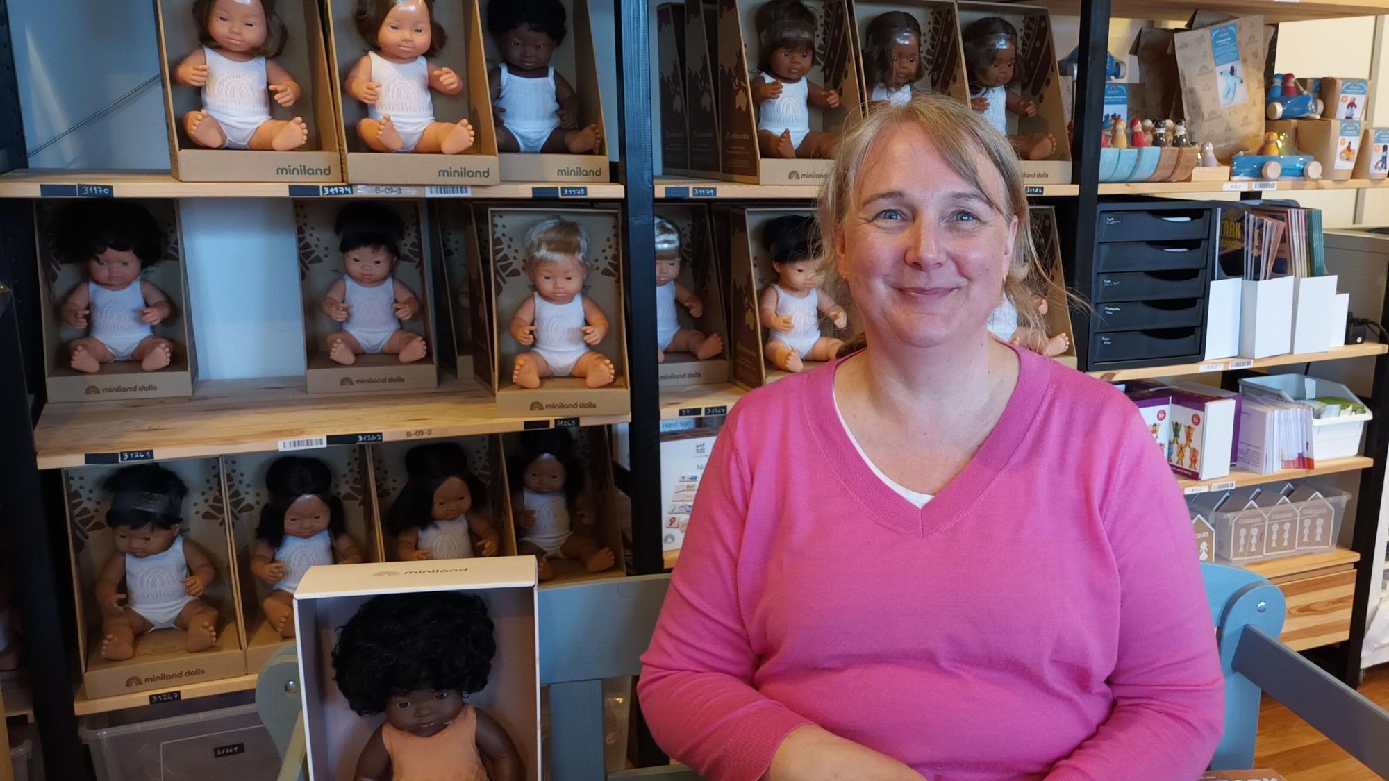 Eine Frau sitzt vor einem Regal mit Puppen unterschiedlicher Hautfarbe
