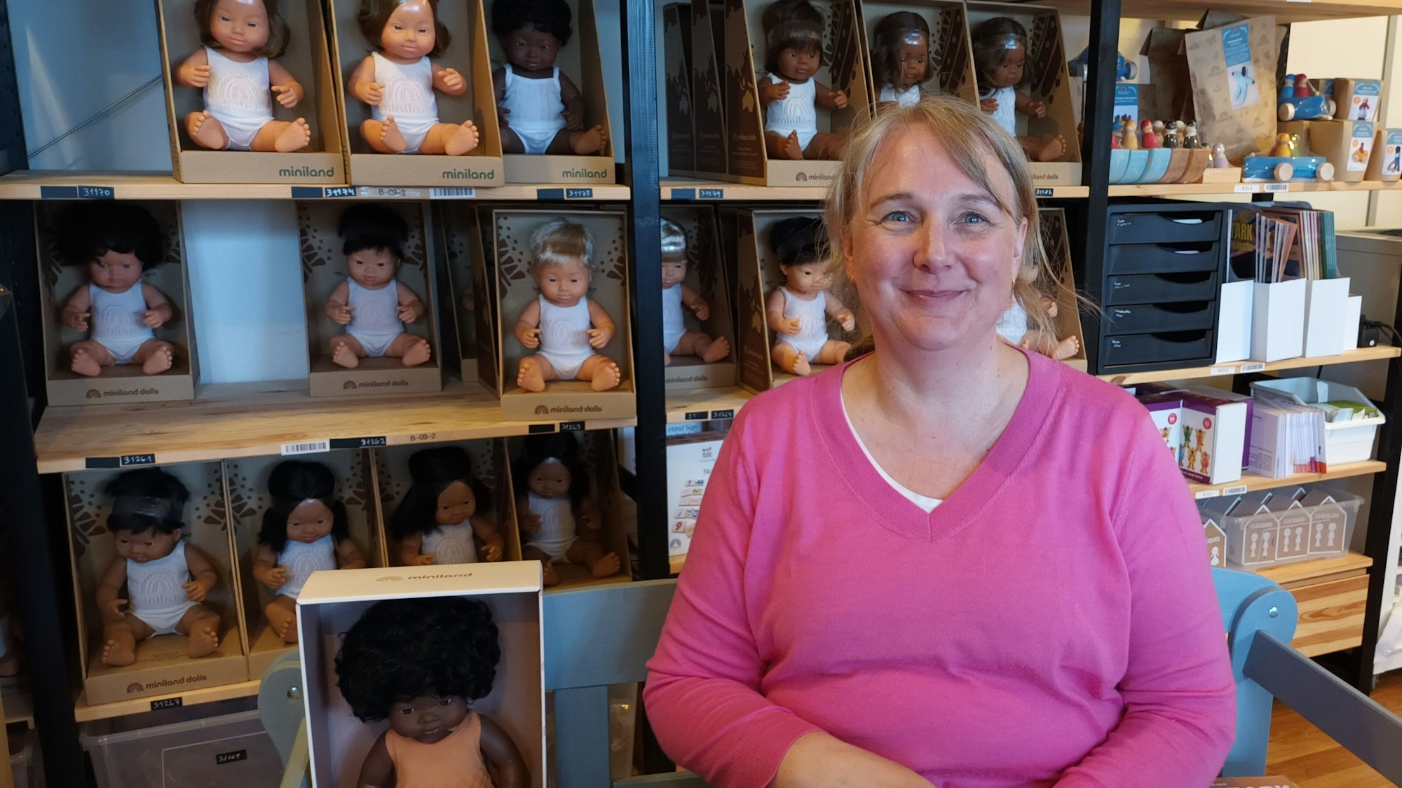 Eine Frau sitzt vor einem Regal mit Puppen unterschiedlicher Hautfarbe