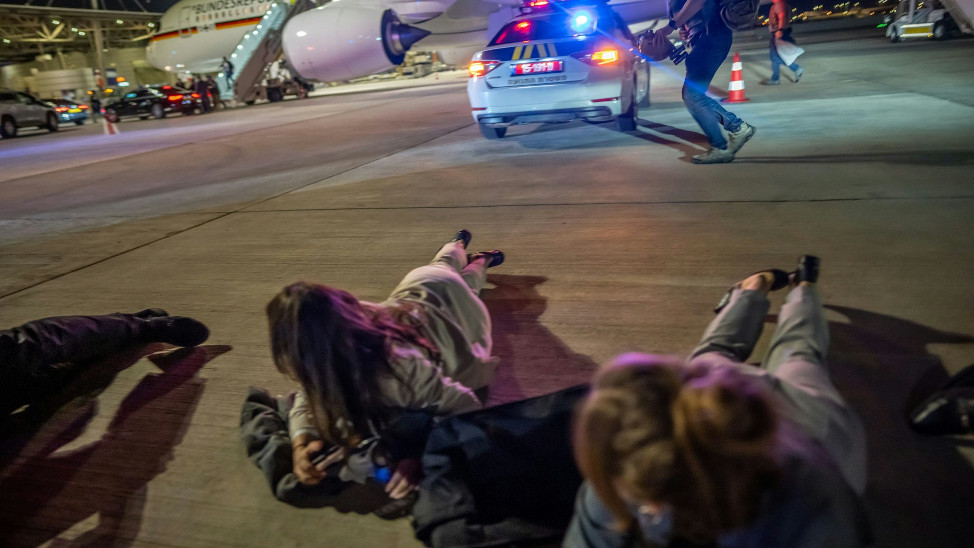 Personen liegen auf dem Flughafen von Tel Aviv vor dem Luftwaffen-Airbus von Bundeskanzler Scholz auf dem Boden. Die Delegation des Bundeskanzlers hatte vor dem Abflug nach Kairo wegen eines Raketenalarms schlagartig das Flugzeug verlassen müssen.