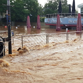 Eines der Ausstellungsbilder zeigt die mit braunem Wasser überflutete Neustraße und den tieferliegenden, vollgelaufenen Herz-Jesu-Vorplatz in Euskirchen.