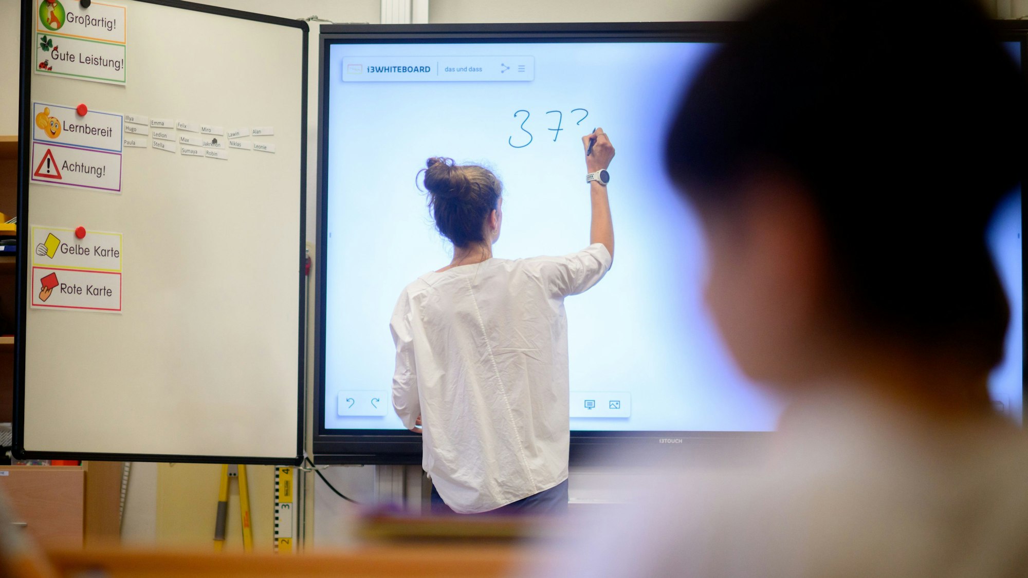 Eine Lehrerin steht mit dem Rücken zur Klasse an einer digitalen Tafel.