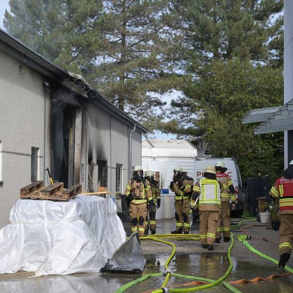 Feuerwehrleute mit Atemschutzausrüstung stehen am Eingang einer verrußten Gewerbehalle.