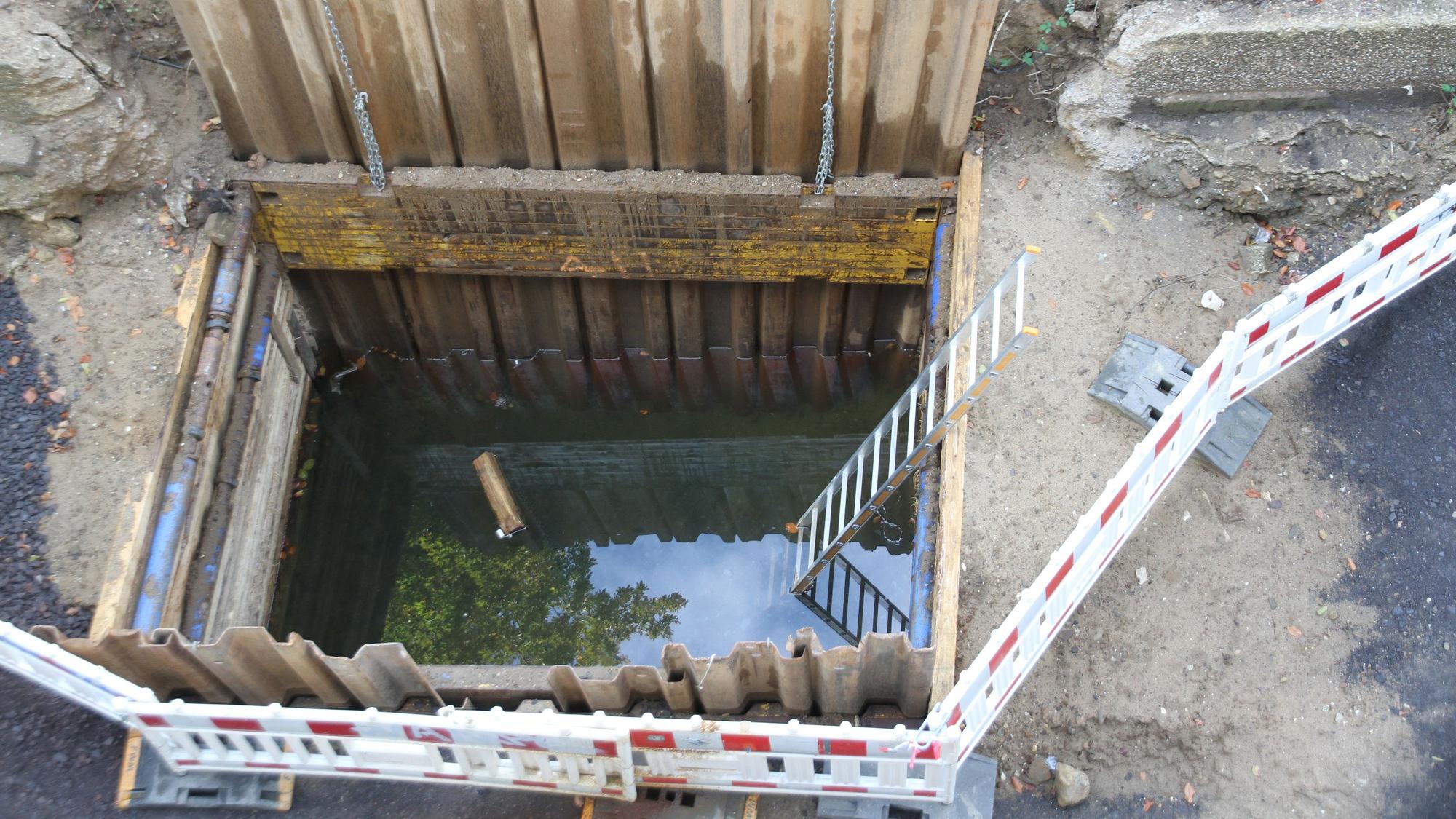 Wasser steht in einem abgesperrten Schacht für eine Regenwasserzisterne.