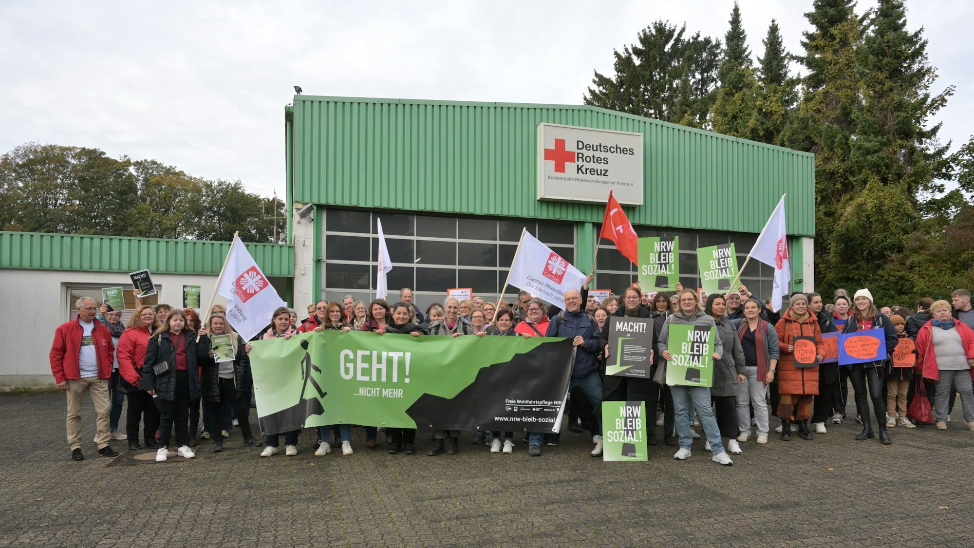 Vor dem Gebäude des DRK haben sich die Demo-Teilnehmer aufgestellt und halten ihre Plakate und Banner hoch.