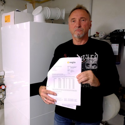 Andreas Kläser steht an seiner Heizungsanlage. In der Hand hält er Rechnungen des Energieversorgers e-regio.