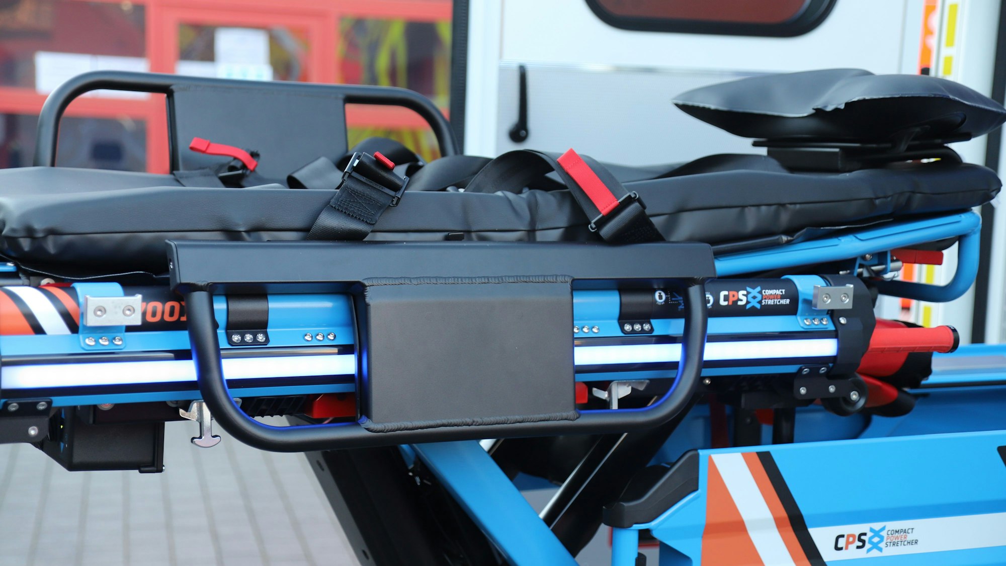 Eine hydraulische Trage steht hinter einem Rettungswagen.