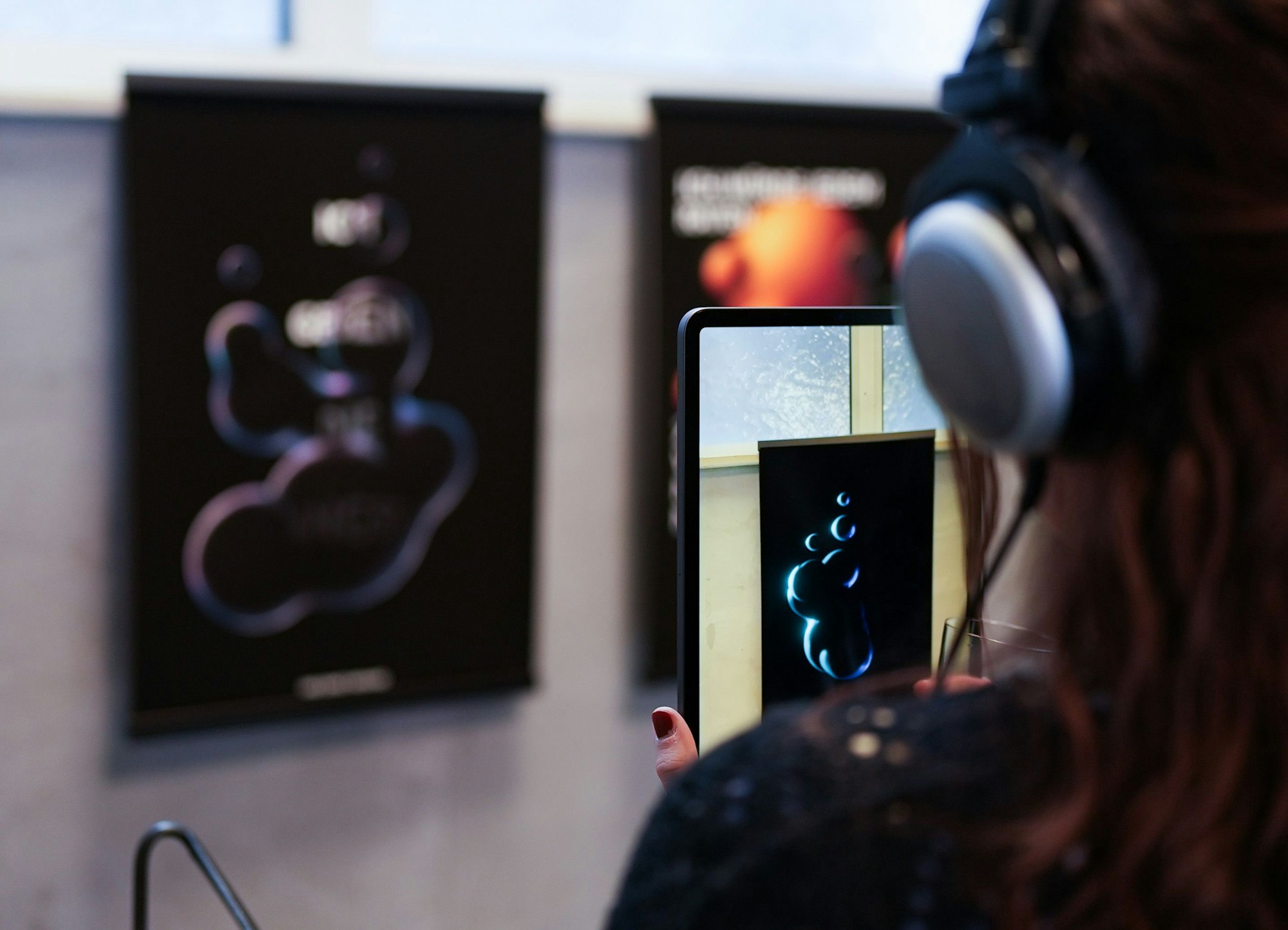 Eine Frau hält ein Tablet vor ein an der Wand hängendes Kunstwerk.