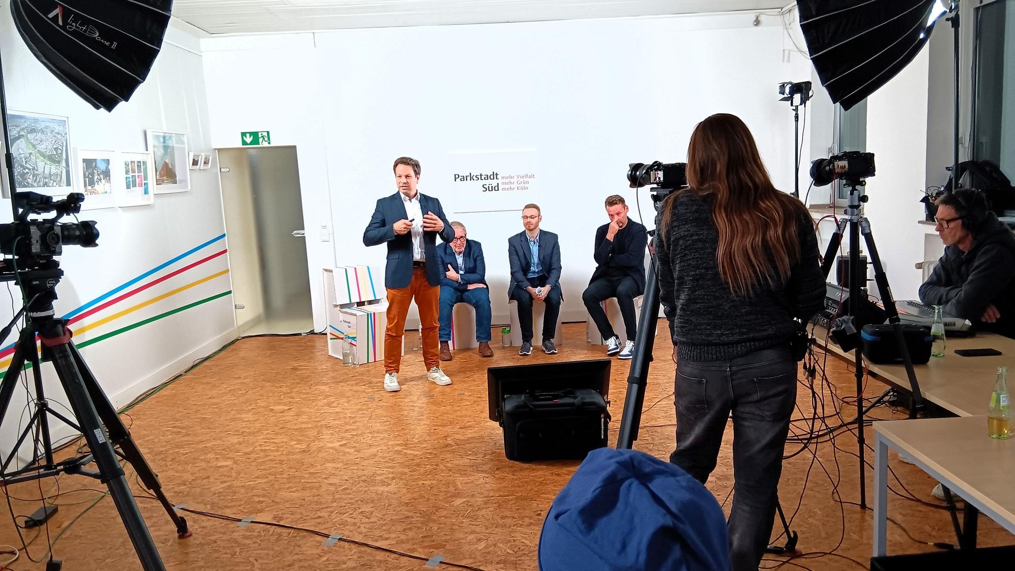 Menschen sitzen auf Hockern und werden gefilmt.