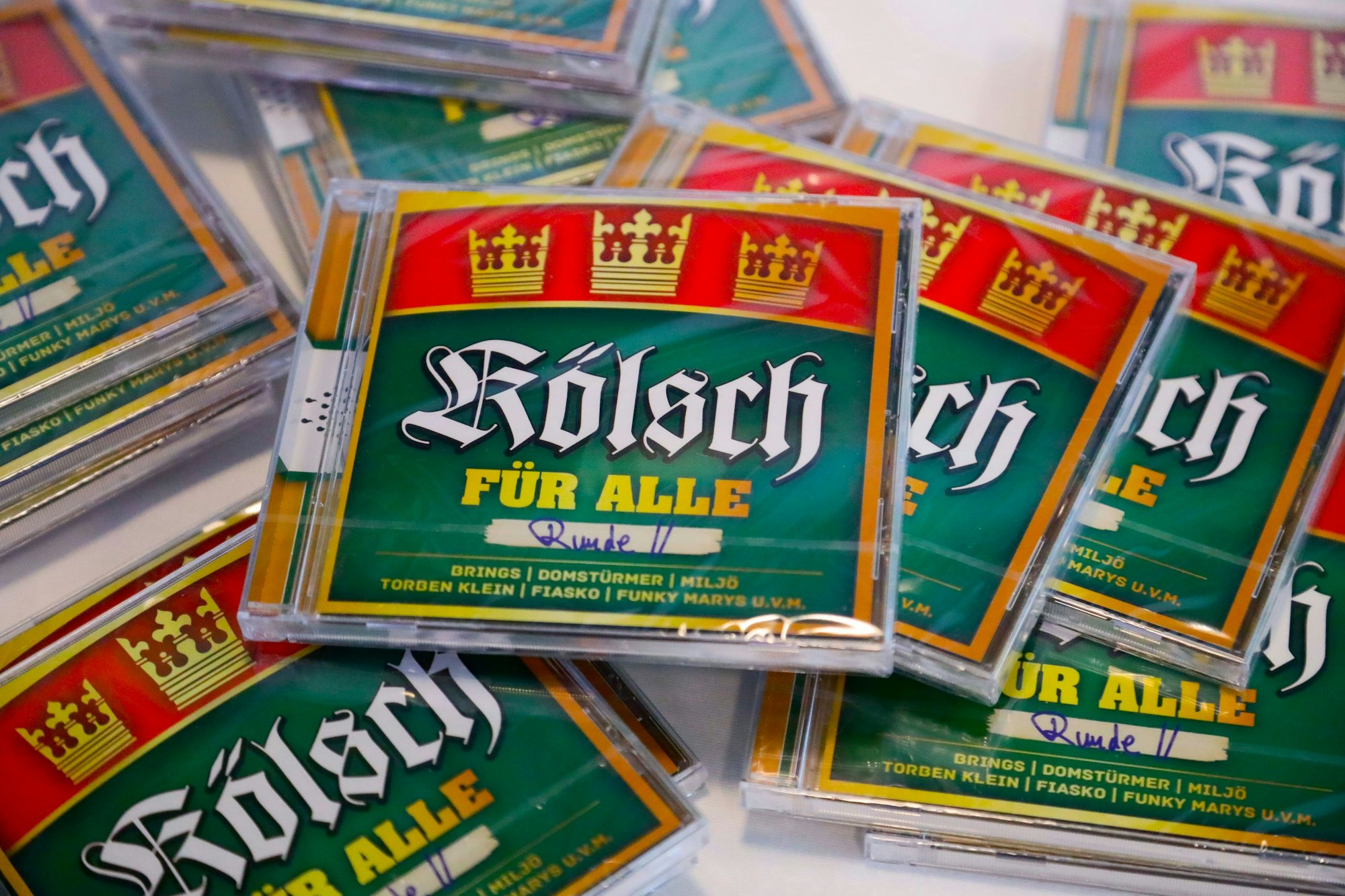 Mehrere CD's „Kölsch für alle – Runde 2“ liegen auf einem Tisch.
