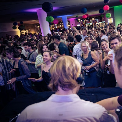 Auf dem Foto ist ein DJ zu sehen, vor ihm eine feiernde Menge.