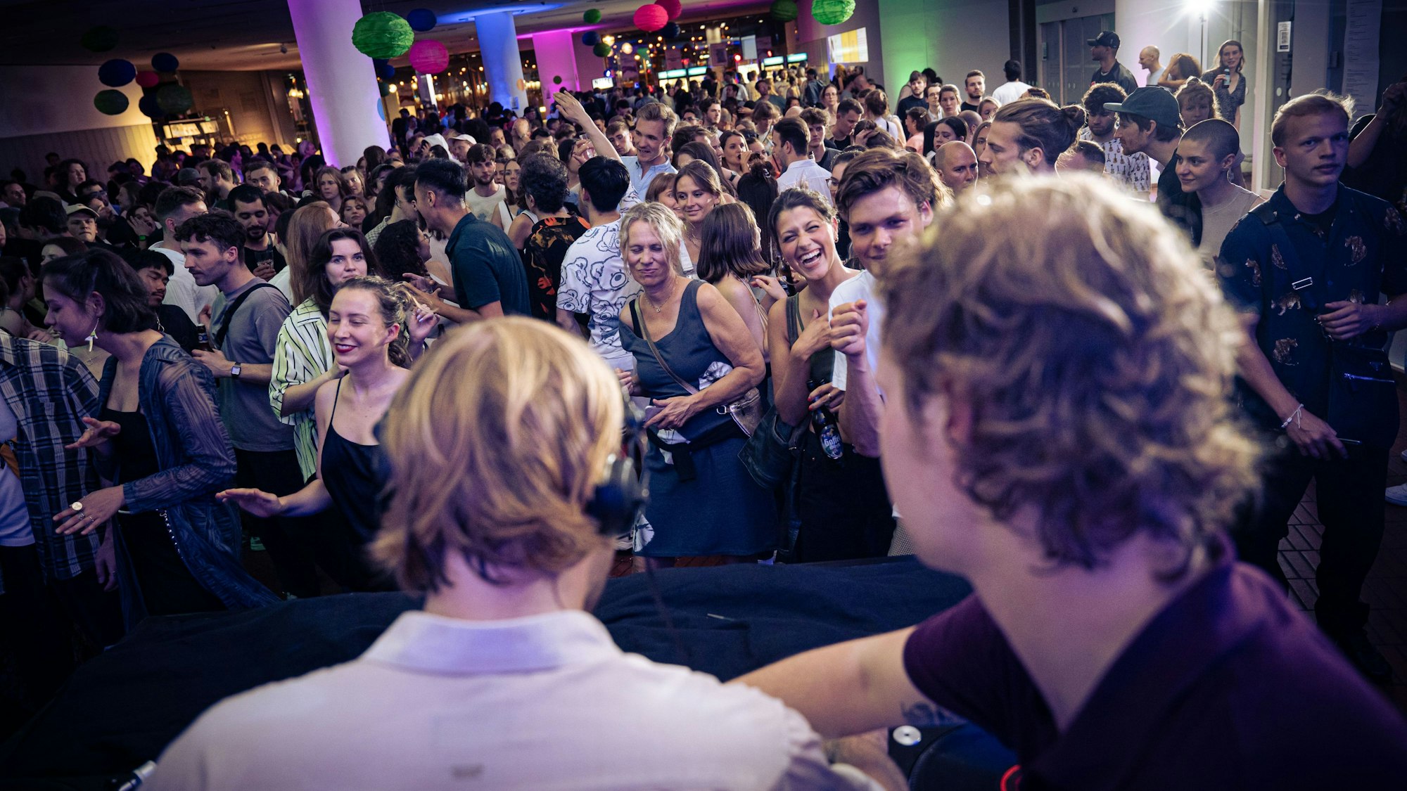 Auf dem Foto ist ein DJ zu sehen, vor ihm eine feiernde Menge.