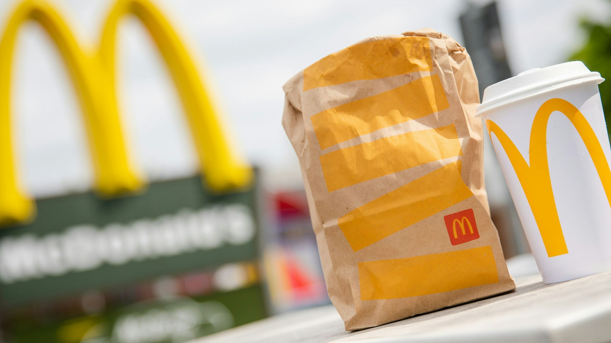 Eine McDonald's To-Go-Tüte und ein To-Go-Becher stehen vor einer Tübinger McDonald's-Filiale.