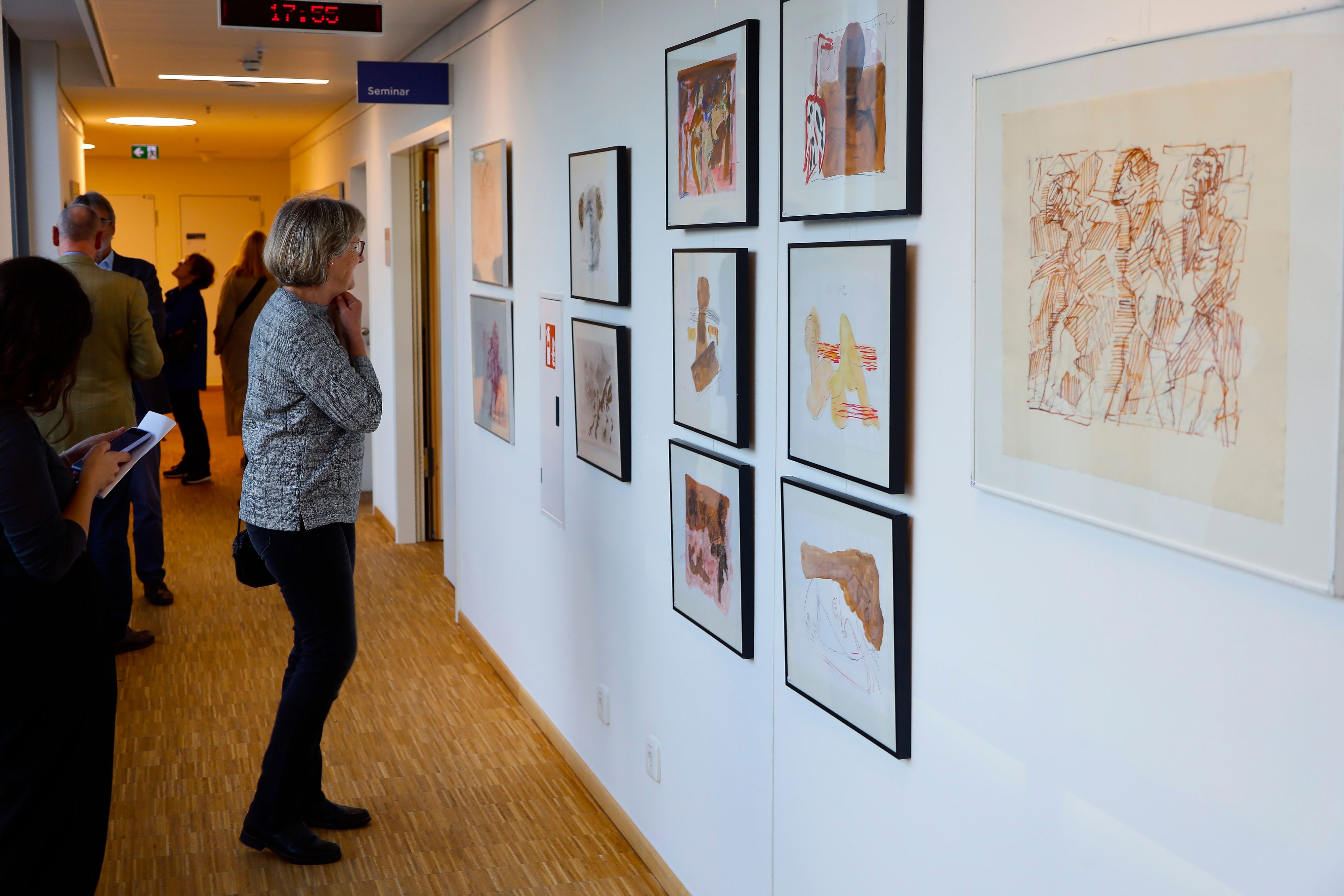 Eine Frau steht vor mehreren Malereien, die an der Wand hängen.