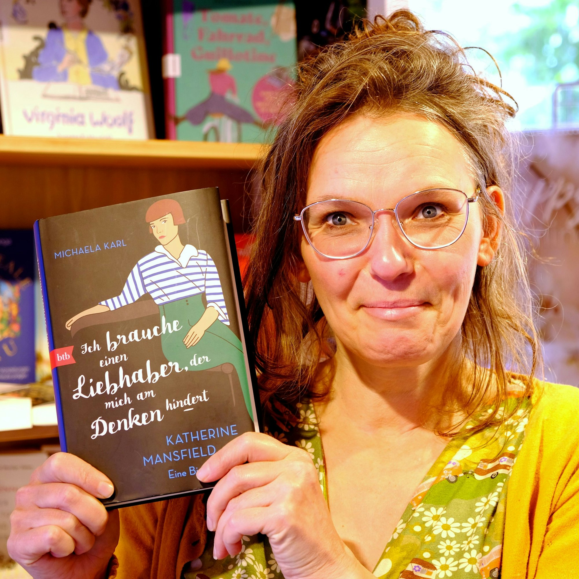 Rosa Wirtz steht mit einem Exemplar des neuen Buchs von Michaela Karl vor einem Bücherregal.