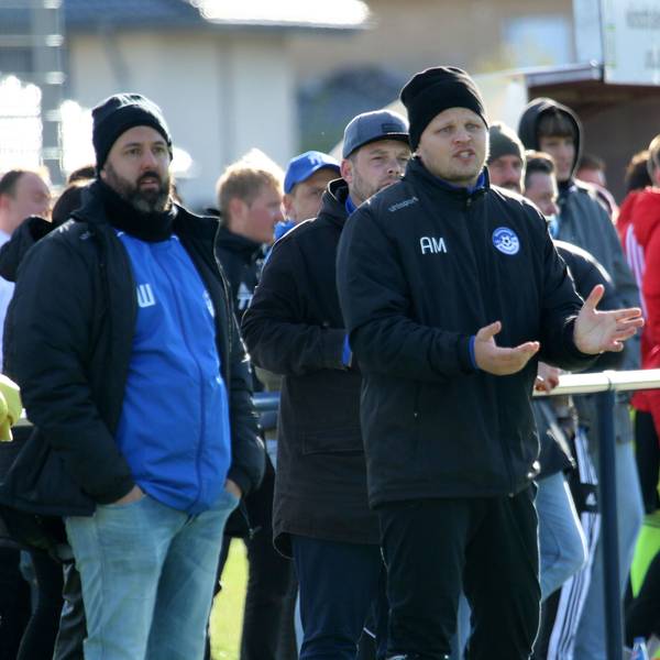 Artur Mezler steht während einer Fußballpartie am Spielfeldrand, hinter ihm Zuschauer.