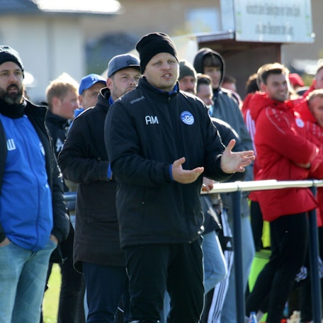 Artur Mezler steht während einer Fußballpartie am Spielfeldrand, hinter ihm Zuschauer.