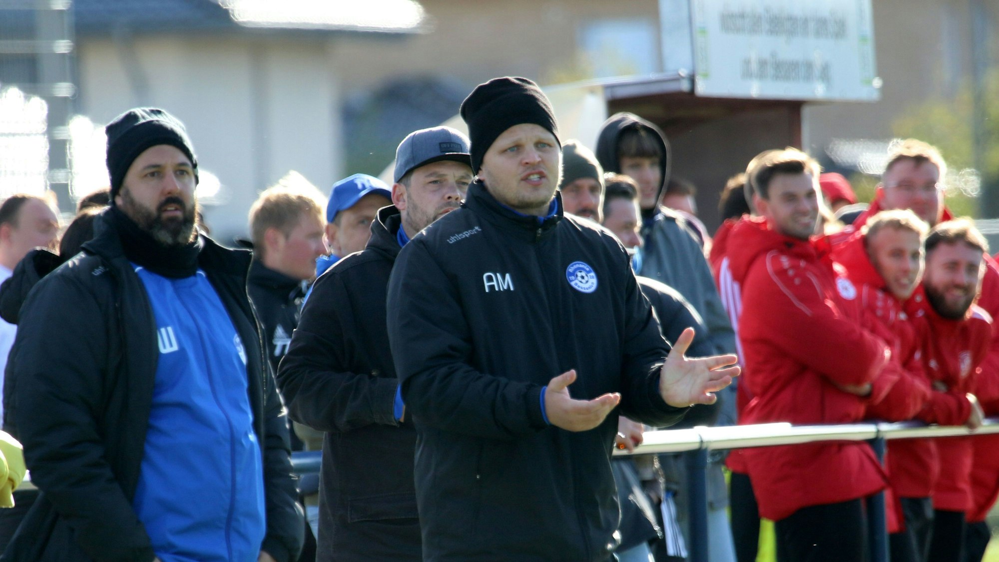 Bessenichs Trainer Artur Mezler (M.) und der Sportliche Leiter Beniamin Warrach (l.) stehen während der Partie gegen Zülpich am Spielfeldrand, hinter ihnen Zuschauer.