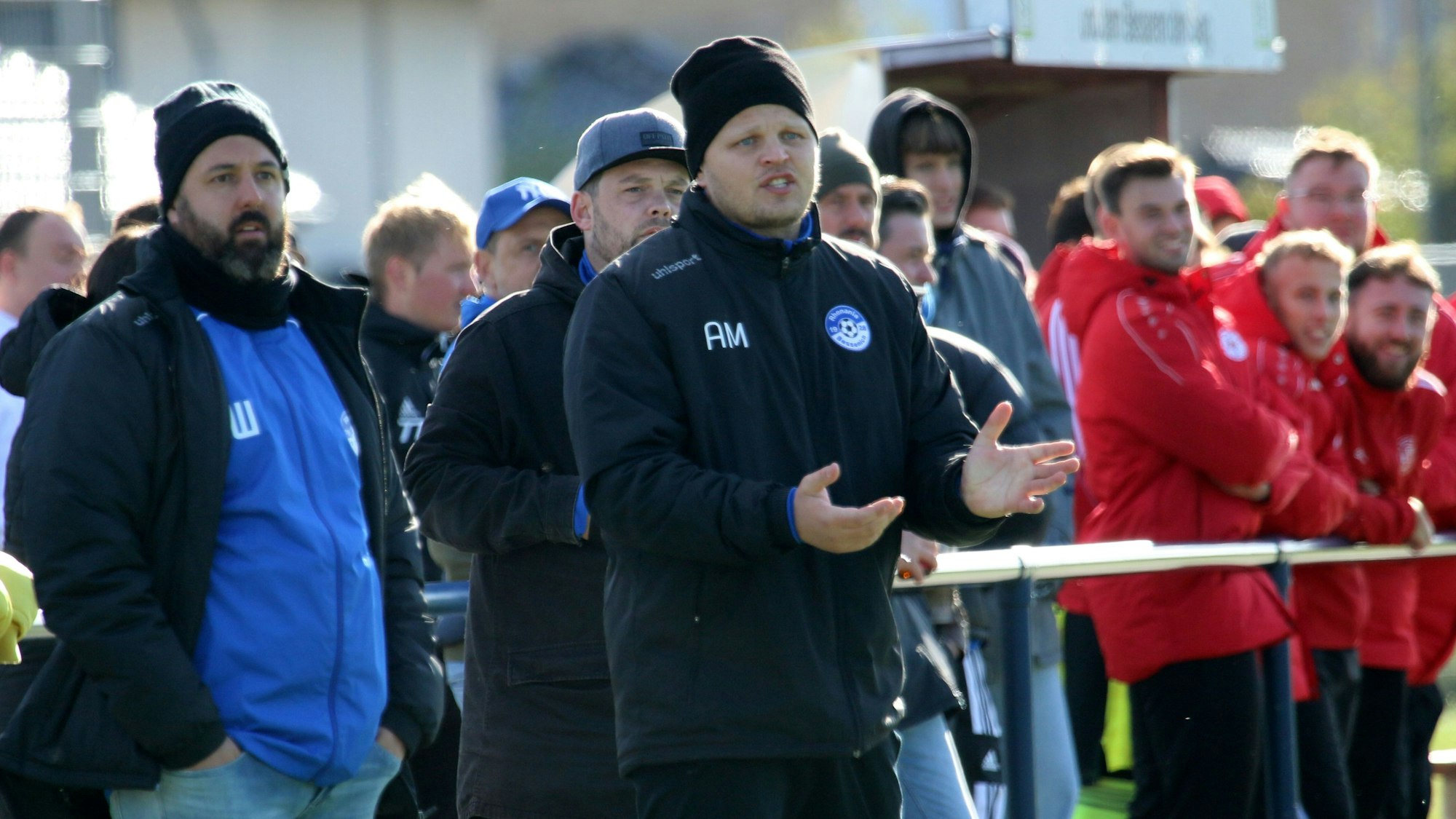 Beniamin Warrach und Trainer Artur Mezler schauen ein Fußballspiel. Es ist alt, beide tragen Mützen.
