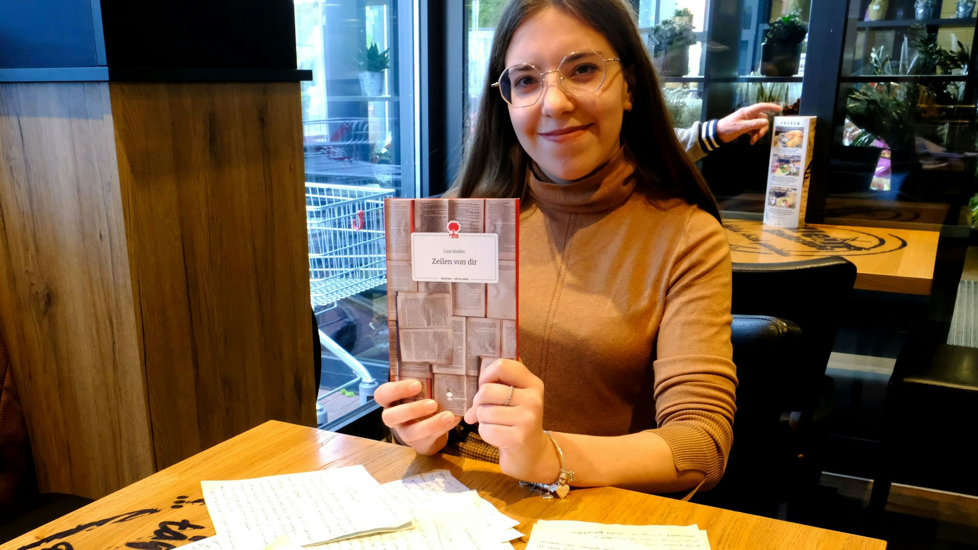 Lina Siedler aus Mechernich präsentiert das Buch über ihre Großeltern. Vor ihr auf dem Tisch liegen einige alte Briefe.