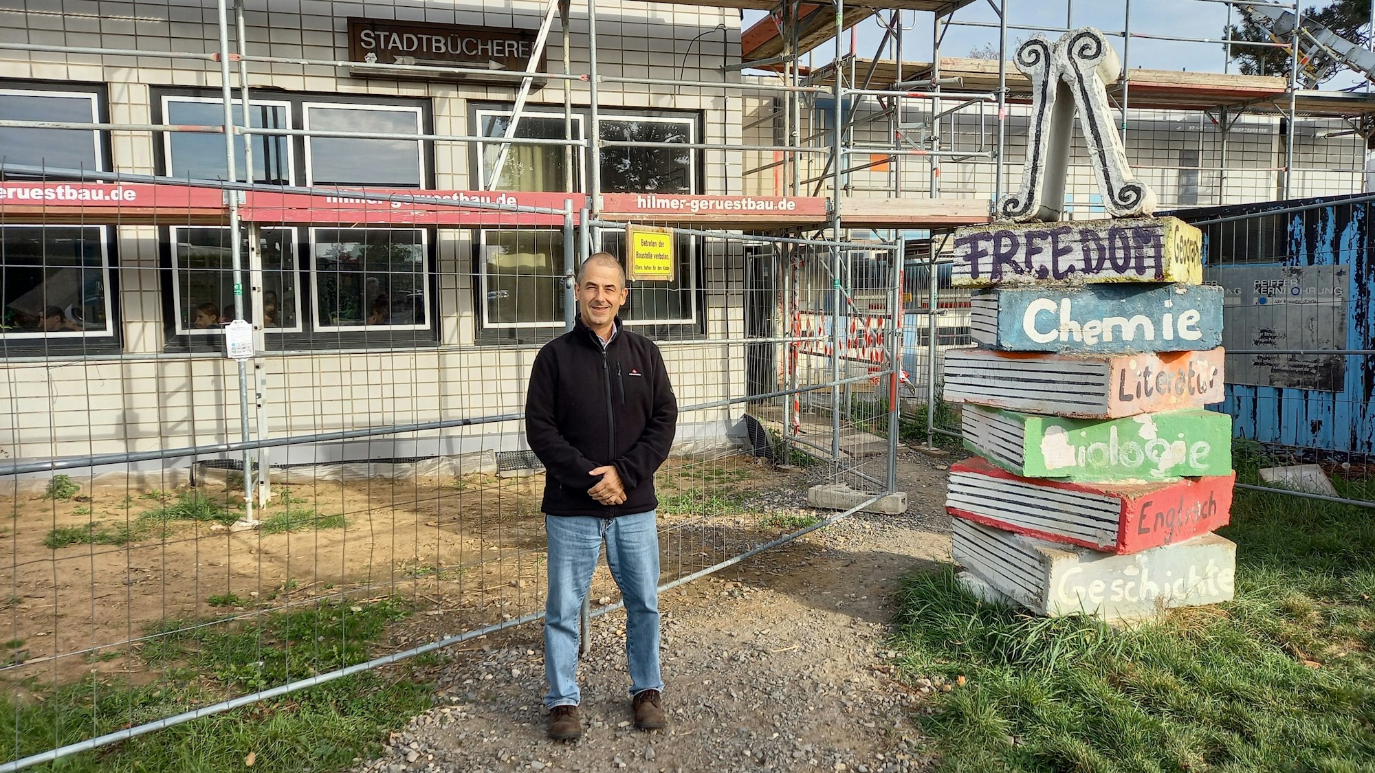 Ein Mann steht vor einem eingerüsteten Gebäude.