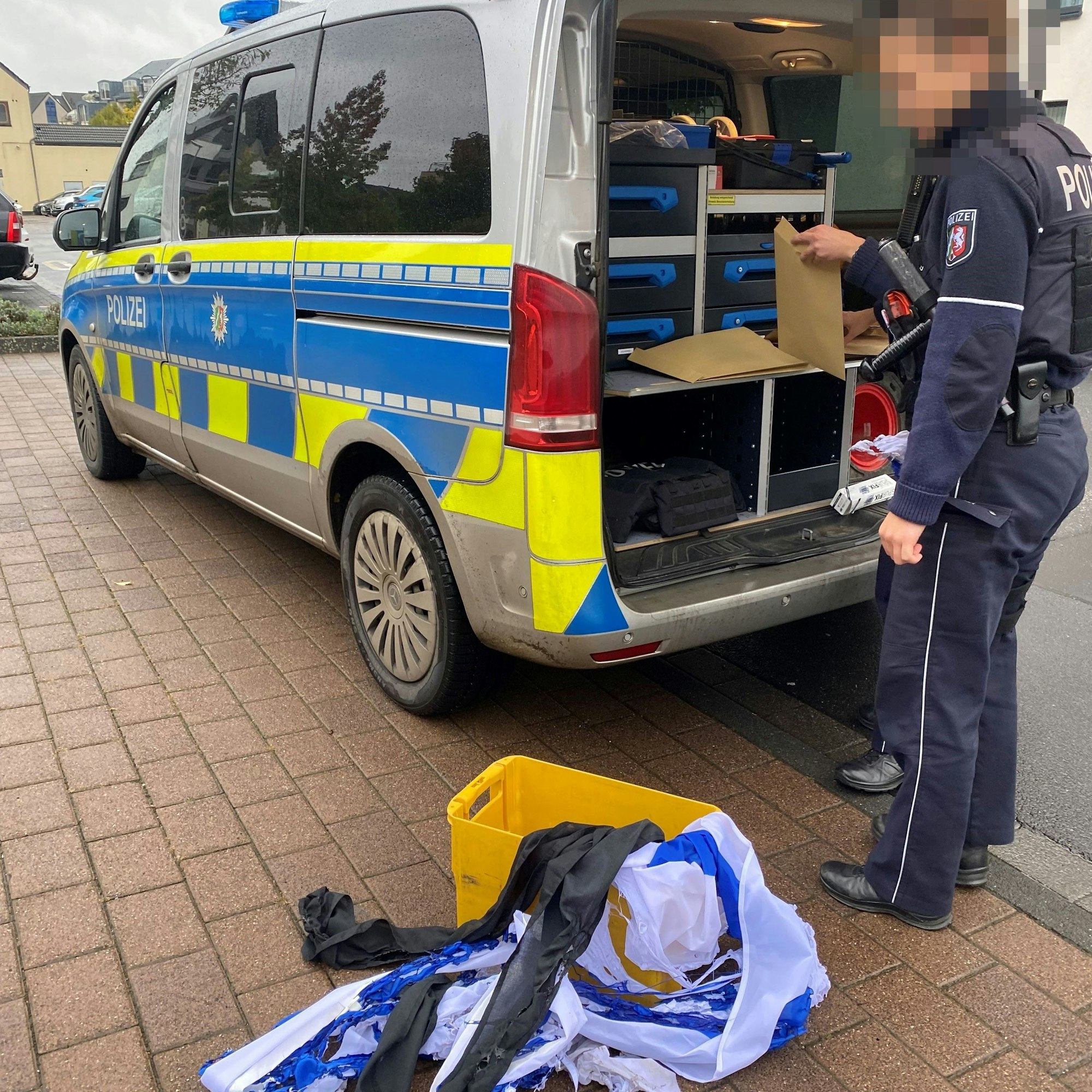 Eine Polizeibeamtin steht an einem Einsatzfahrzeug. Reste einer in Brand gesetzten israelischen Flagge liegen davor auf dem Boden.