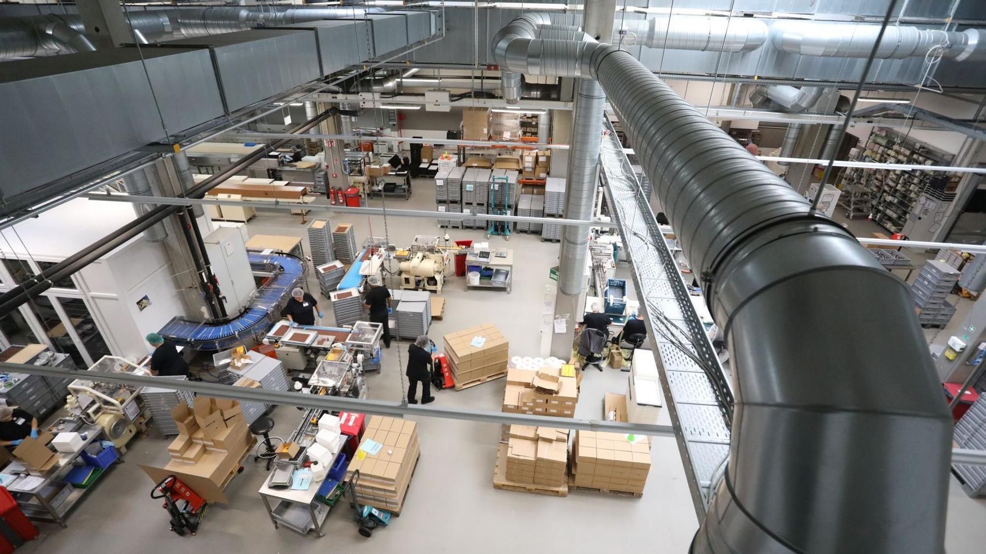 Blick von oben in die Produktionshalle der Confiserie mit diversen Apparate, Fließbändern, Kartons, Mitarbeitern und Lüftungsrohren.