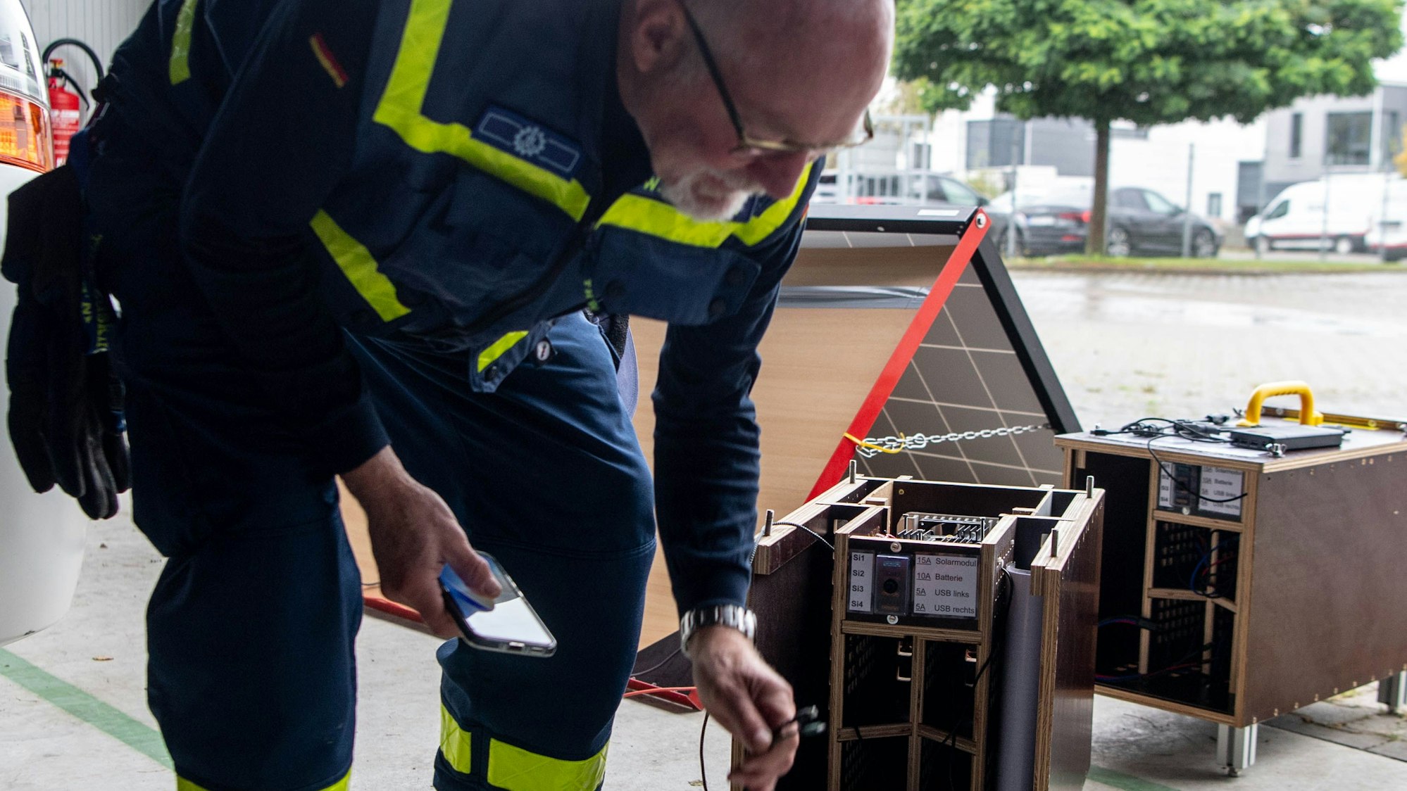 Das Bild zeigt Wolfgang Bremer, wie er zwei Aufladekabel in der linken Hand hält. In der Rechten hält er sein Smartphone.