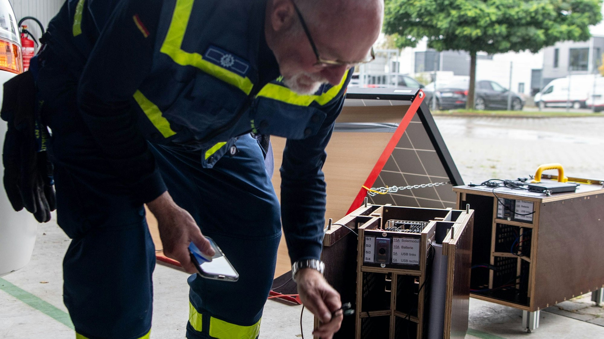Das Bild zeigt Wolfgang Bremer, wie er zwei Aufladekabel in der linken Hand hält. In der Rechten hält er sein Smartphone.
