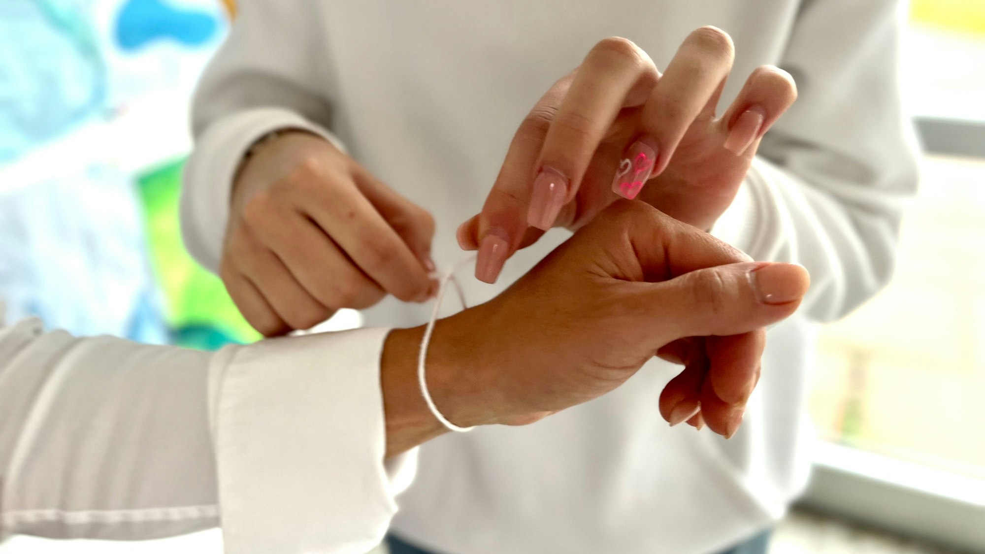 Ein Mädchen bindet einem andern ein weißes Band ums Handgelenk.