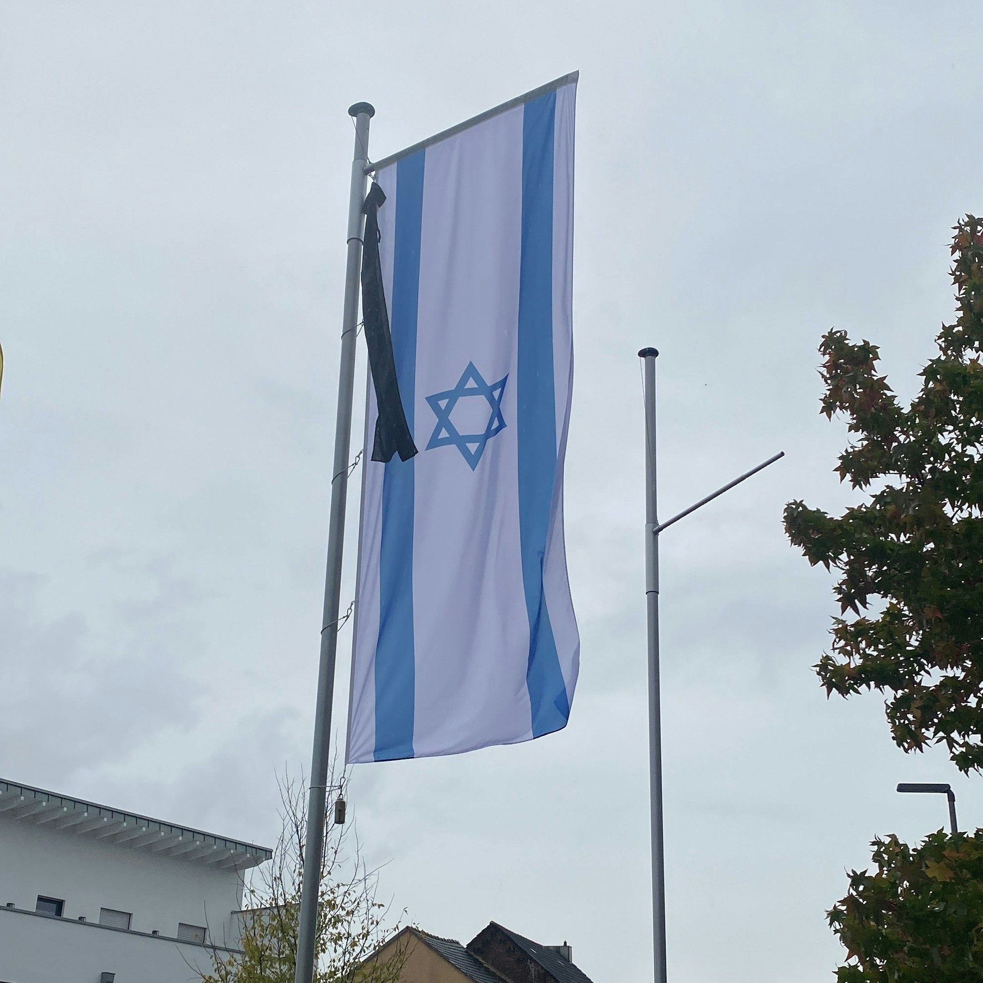 An einem Fahnenmast hängt eine israelische Fahne. Sie ist mit einem Trauerflor geschmückt.