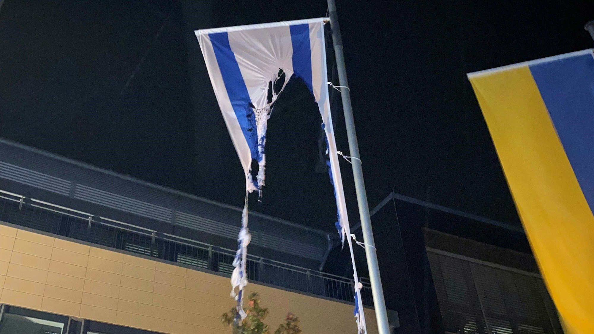 Die Reste einer israelischen Flagge, die an einem Fahnenmast vor dem Rathaus in Mechernich hängt, ist zu großen Teilen verbrannt. Daneben ist eine ukrainische Fahne zu sehen.