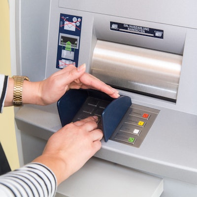 Eine Person gibt die Geheimzahl ihrer Zahlungskarte an einem Geldautomaten ein.