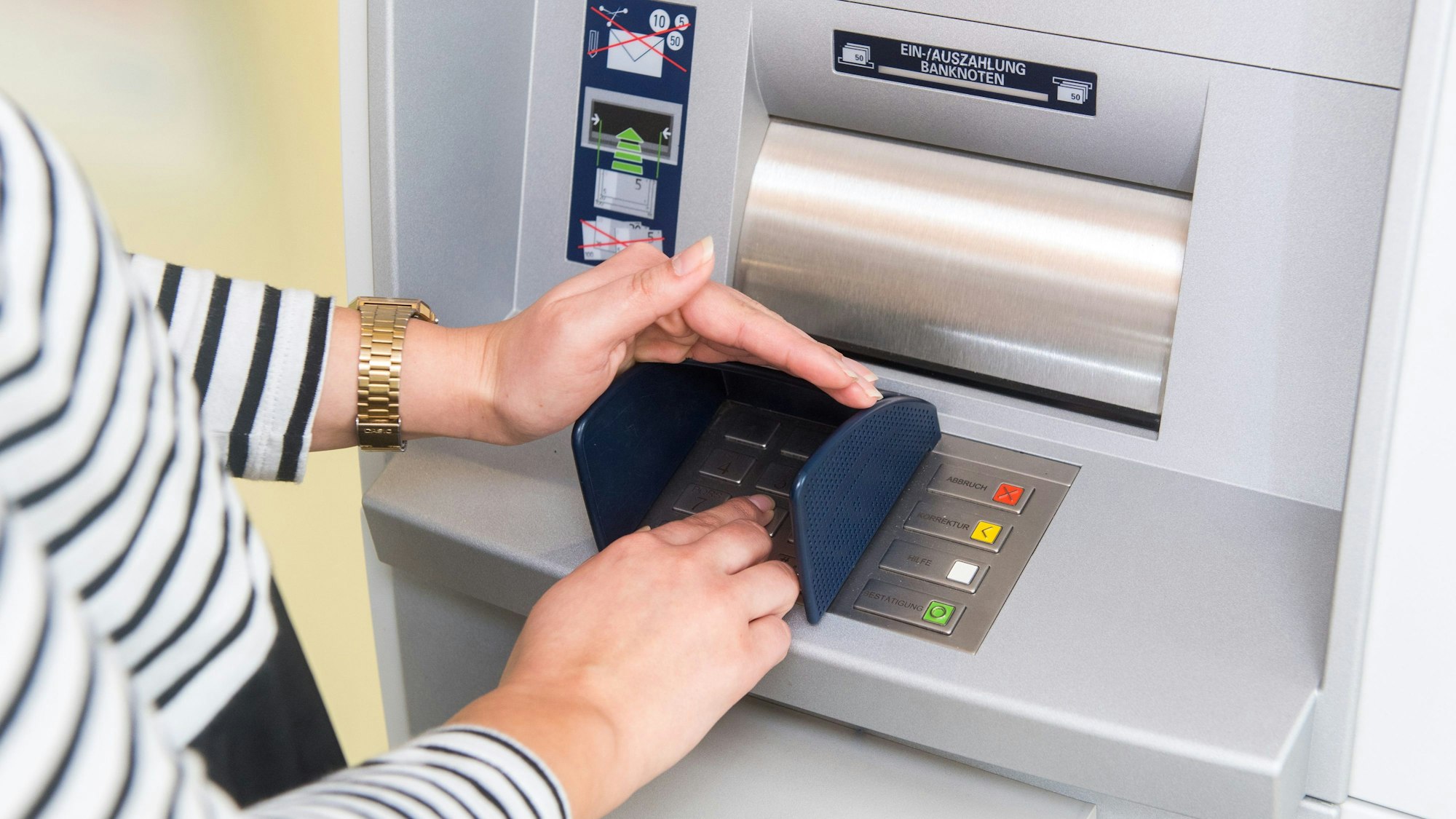 Eine Person gibt die Geheimzahl ihrer Zahlungskarte an einem Geldautomaten ein.