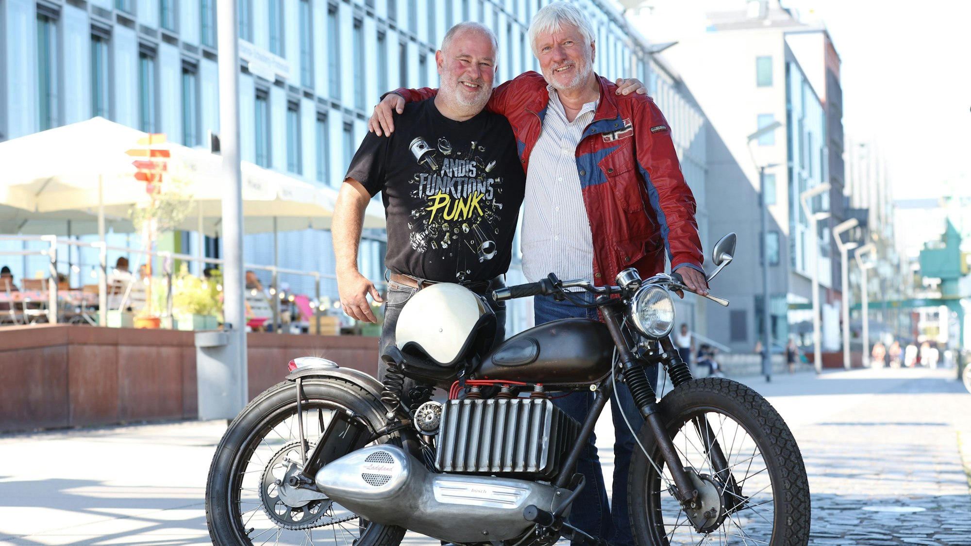 Jürgen Becker und Klaus Mittendorfer stehen Arm in Arm vor ihrem Motorrad.