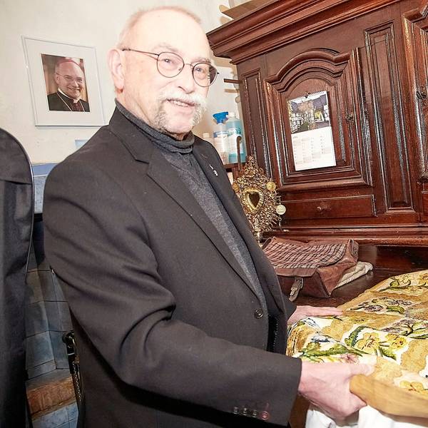 Pfarrer Philipp Cuck steht in der Sakristei, im Hintergrund hängt ein Bild, das den Aachener Bischof Dr. Helmut Dieser zeigt.