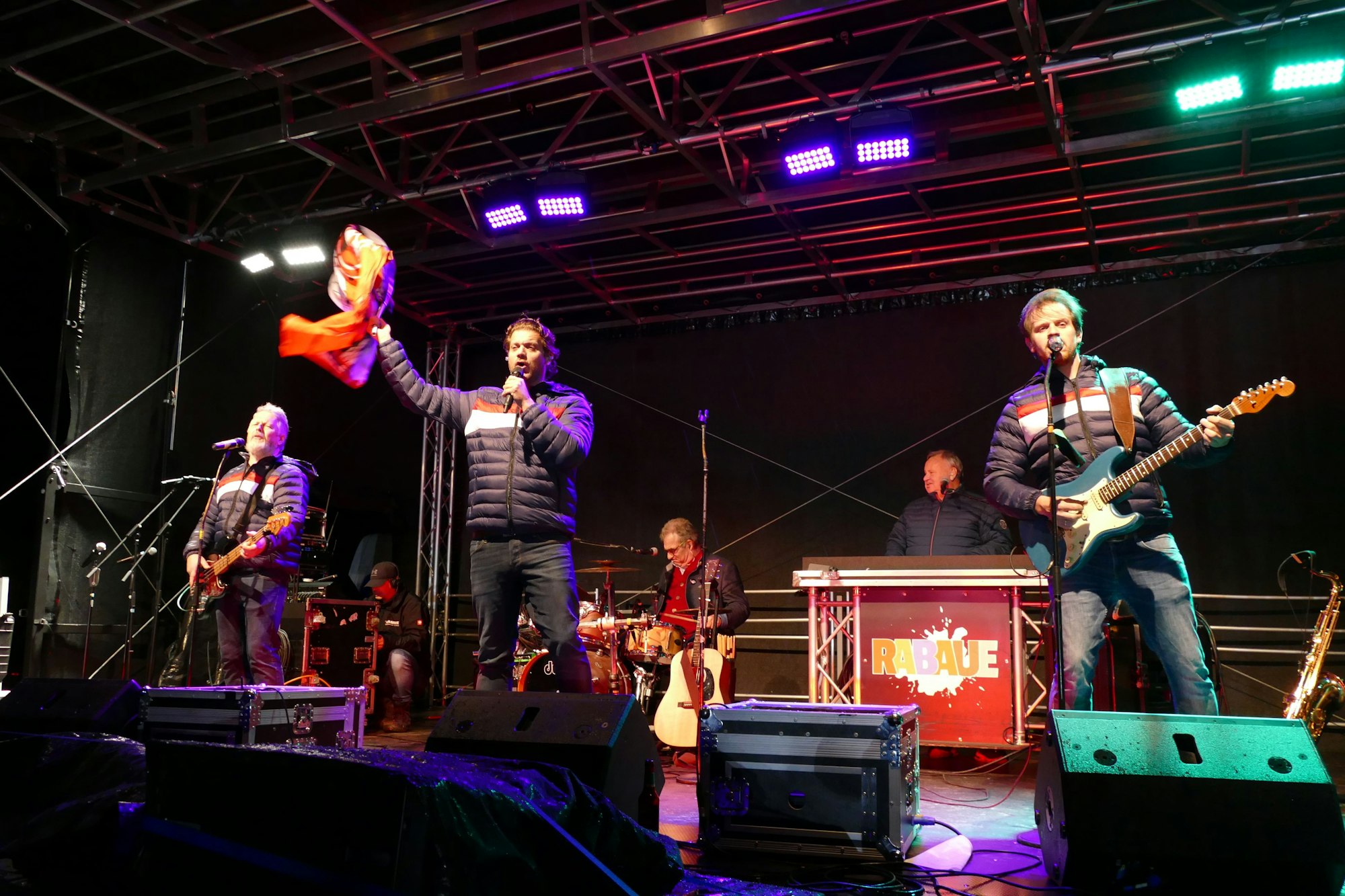 Drei Musiker stehen auf einer Bühne, einer schwenkt eine Fahne des 1. FC Köln